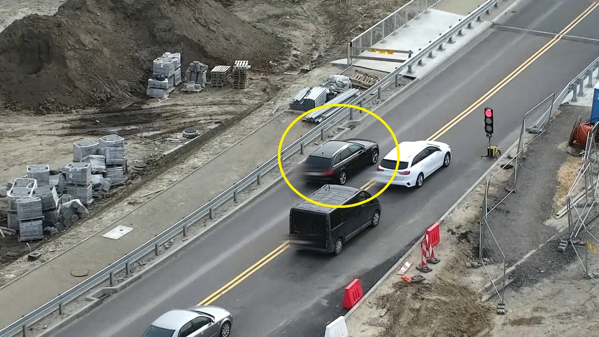 Ujęcie z policyjnego drona na którym widac osobowe auto przejeżdżające na czerwonym świetle.