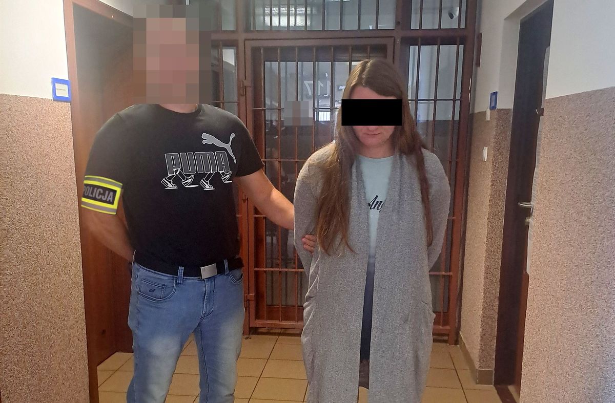 Policjant prowadzi zatrzymaną kobietę.