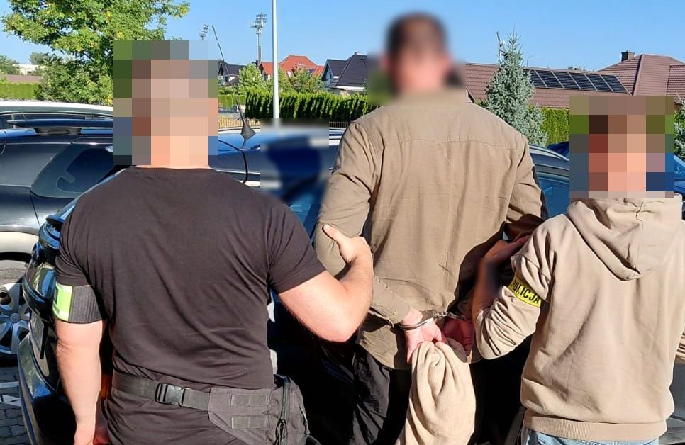 Dwóch policjantów prowadzi do radiowozu zatrzymanego mężczyznę.
