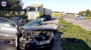 rozbity pojazd osobowy widziany z przodu stojący na drodze oraz w tle rozbity pojazd ciężarowy, radiowóz i helikopter