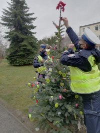 policjanci wieszający elementy odblaskowe na choince ozdobionej odblaskami