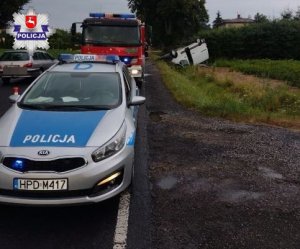 radiowóz policyjny i wóz straży pożarnej stojący na drodze i auto koloru białego na dachu w rowie