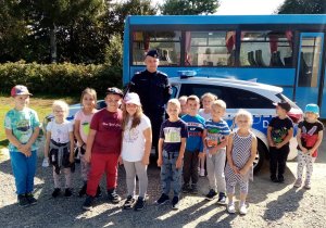 policjant z dziećmi na tle radiowozu i autobusu szkolnego