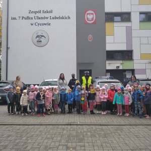 dzieci i policjanci stojący na tle radiowozu i budynku szkolnego