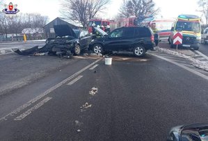 dwa rozbite auta koloru ciemnego stojące na drodze za nimi dwa ambulansy i dwa pojazdy strażackie