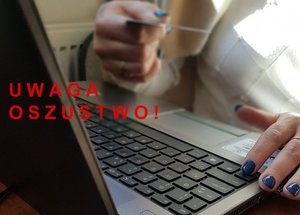 Ręka trzymająca kartę bankomatowa na tle laptopa oraz napis Uwaga oszustwo!