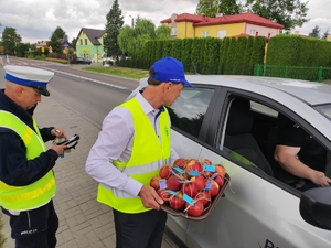 przedstawiciel Państwowej Inspekcji Pracy trzyma tace z jabłkami i przekazuje jabłko kierującemu, obok stoi policjant z łęczyńskiej drogówki