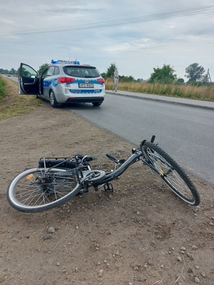 rower leżący na poboczu, w oddali radiowóz