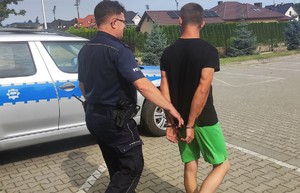 policjant doprowadza zatrzymanego w tle radiowóz