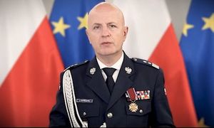 zdjęcie Komendanta Głównego Policji w galowym mundurze. Z tyłu widoczne są flagi Polski i Unii Europejskiej