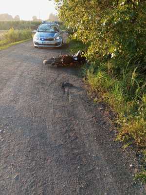 przewrócony motocykl na drodze żużlowej, na drugim planie radiowóz