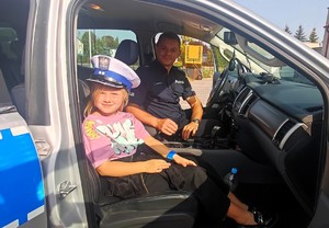 policjant i dziewczynka w policyjnej czapce w radiowozie
