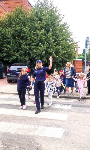 policjantka z dziećmi przechodzą przez przejście dla pieszych