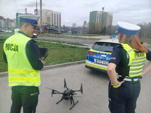 Radiowóz policyjny na tle miasta, dron i dwójka policjantów ruchu drogowego