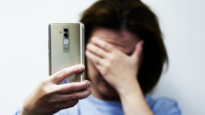 kobieta jedną ręką trzyma telefon, drugą zasłania oczy