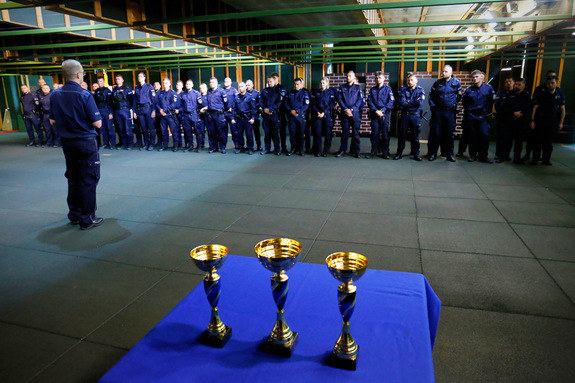 Funkcjonariusze ubrani w mundur koloru granatowego z napisami policja biorący udział w turnieju. Zdjęcie wykonane na strzelnicy policyjnej, gdzie policjanci zapoznają się z regulaminem turnieju.