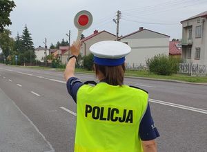 policjantka drogówki z wyciągniętą ręka trzymającą tarczę do zatrzymania pojazdów