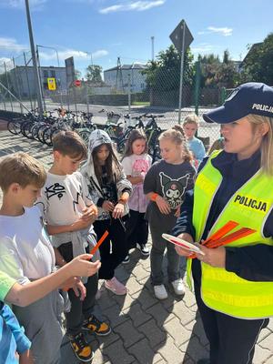 policjantka z dziećmi rozdająca elementy odblaskowe