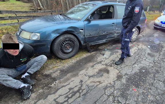 41-latek siedzący przy samochodzie. Obok policjant