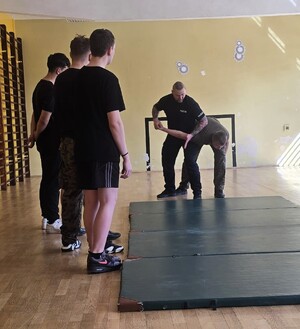 policjant z uczniami podczas prowadzonych zajęć, prezentuje techniki obezwładniania