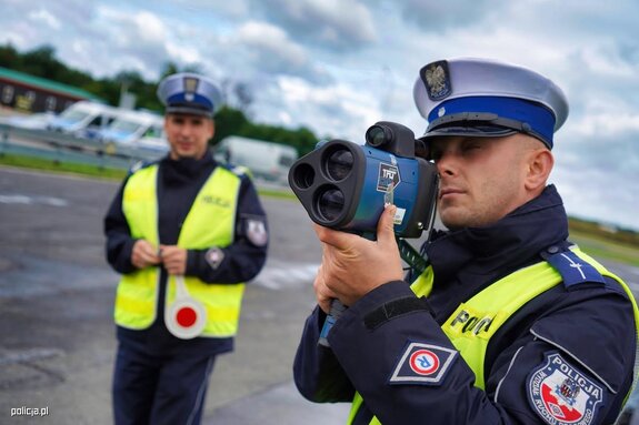 dwóch policjantów na drodze, jeden mierzy prędkość